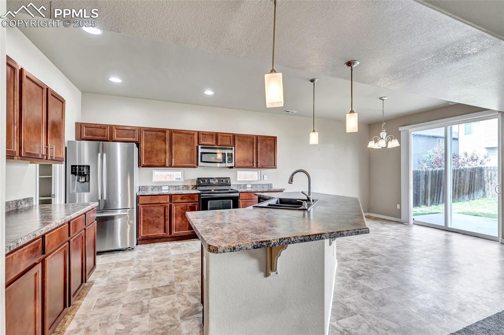 Kitchen featuring stainless steel appliances, decorative light fixtures, a kitchen breakfast bar, brown cabinetry, and recessed lighting