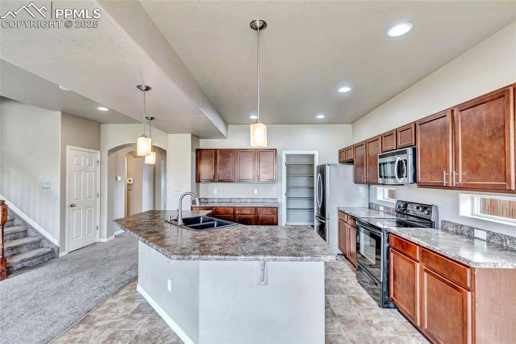 Kitchen with stainless steel appliances, recessed lighting, arched walkways, decorative light fixtures, and brown cabinetry