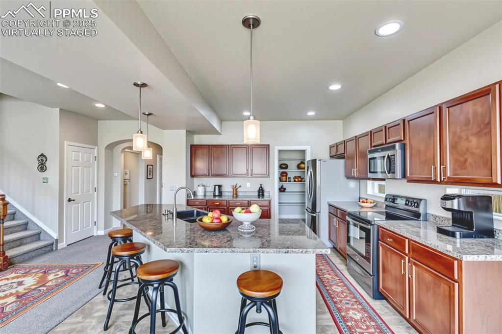 Virtually Staged - Kitchen with appliances with stainless steel finishes, a kitchen bar, recessed lighting, pendant lighting, and arched walkways