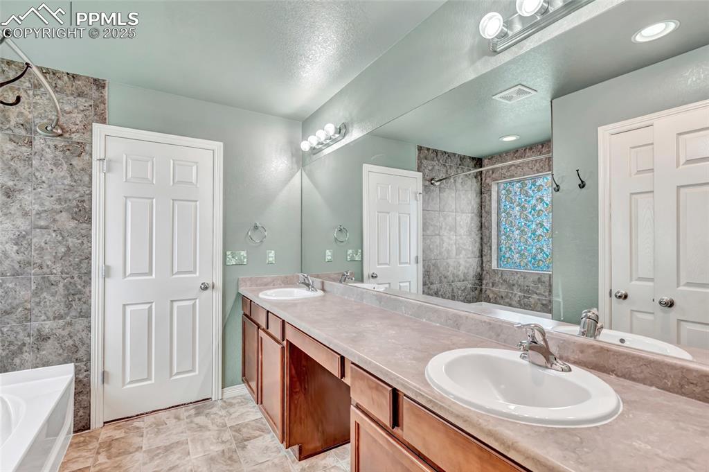 Master bathroom with double vanity, tiled shower / bath, and a textured ceiling