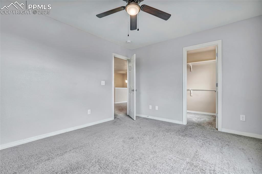 Secondary bedroom featuring a walk in closet, light carpet, and a ceiling fan