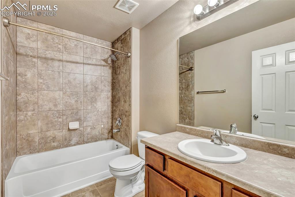Shared bathroom with tub-shower combo combination, vanity, light tile patterned floors, and a textured wall