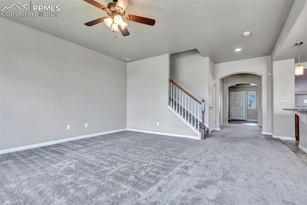 Unfurnished living room with arched walkways, light carpet, stairway, ceiling fan, and recessed lighting