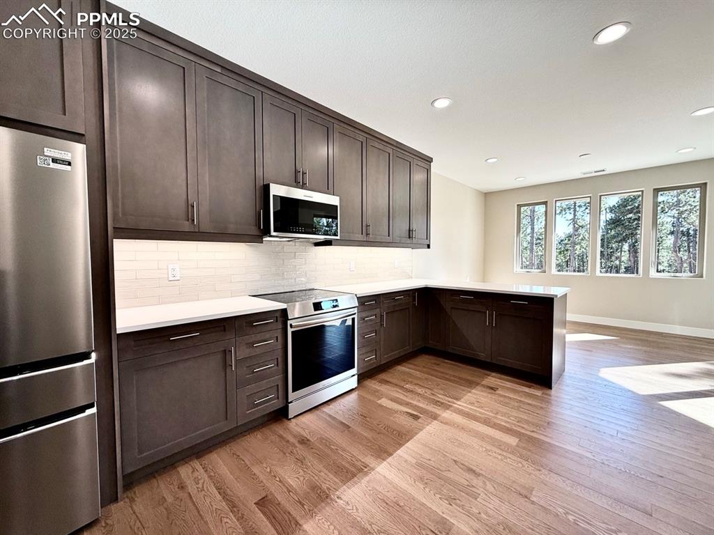 Full-sized Gourmet Kitchen with Quartz Countertops, Induction Range, Cabinetry to the Ceiling, Under-cabinet Lighting, Included Stainless Steel Fridge, and Wood Flooring.