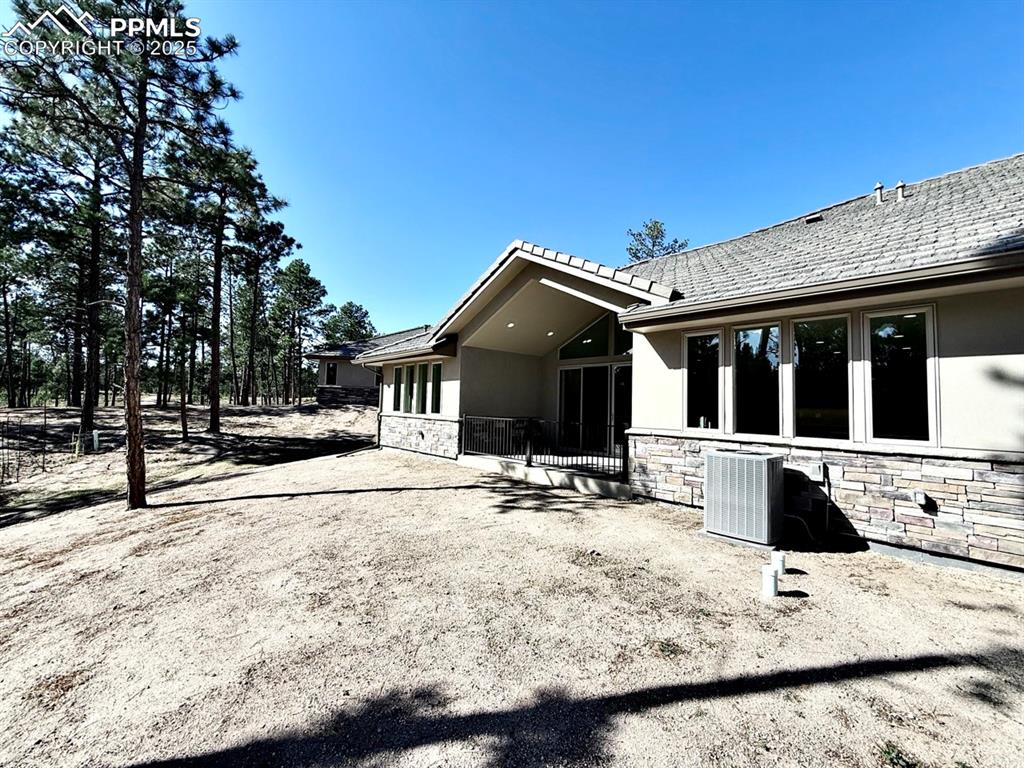 Rear view of house with stone siding, stucco siding, and a patio area