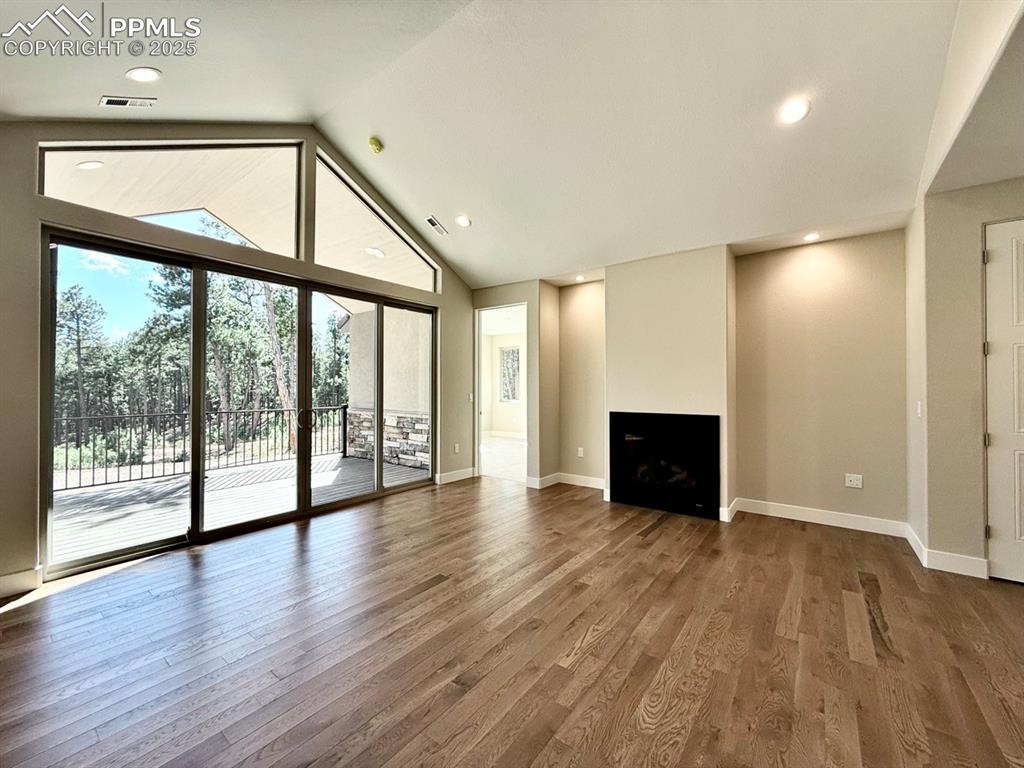 Vaulted Living Room with Gas Fireplace, Oversized Sliding Doors to Covered Composite Deck, and Wood Flooring.