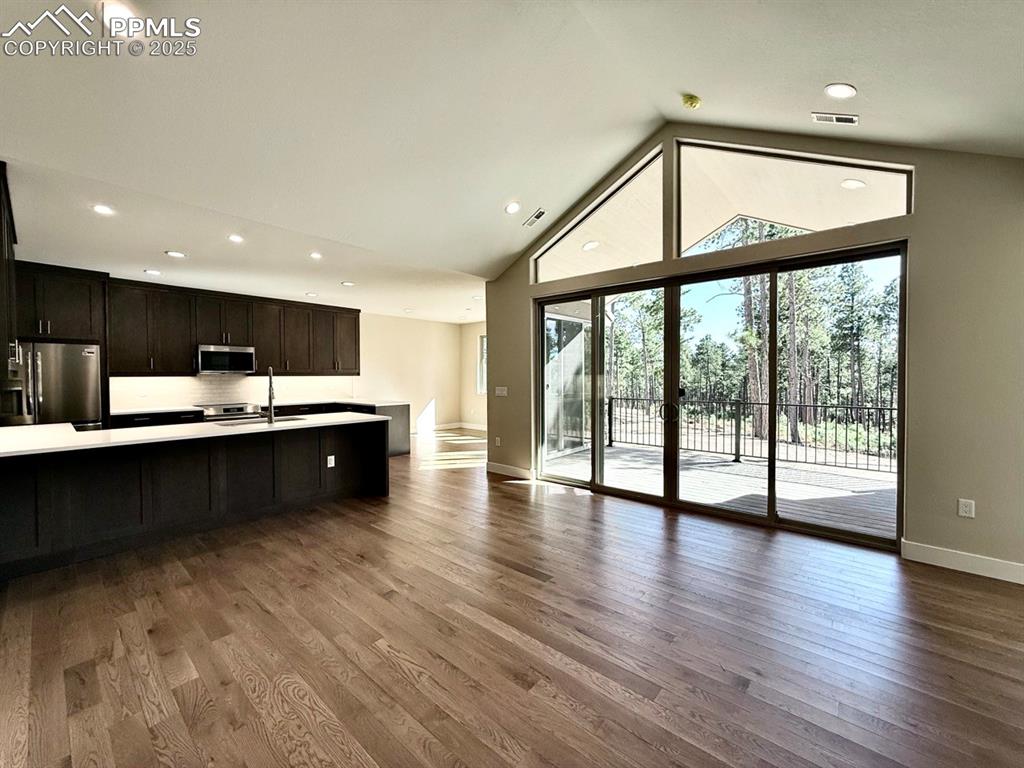 Vaulted Living Room with Gas Fireplace, Oversized Sliding Doors to Covered Composite Deck, and Wood Flooring.