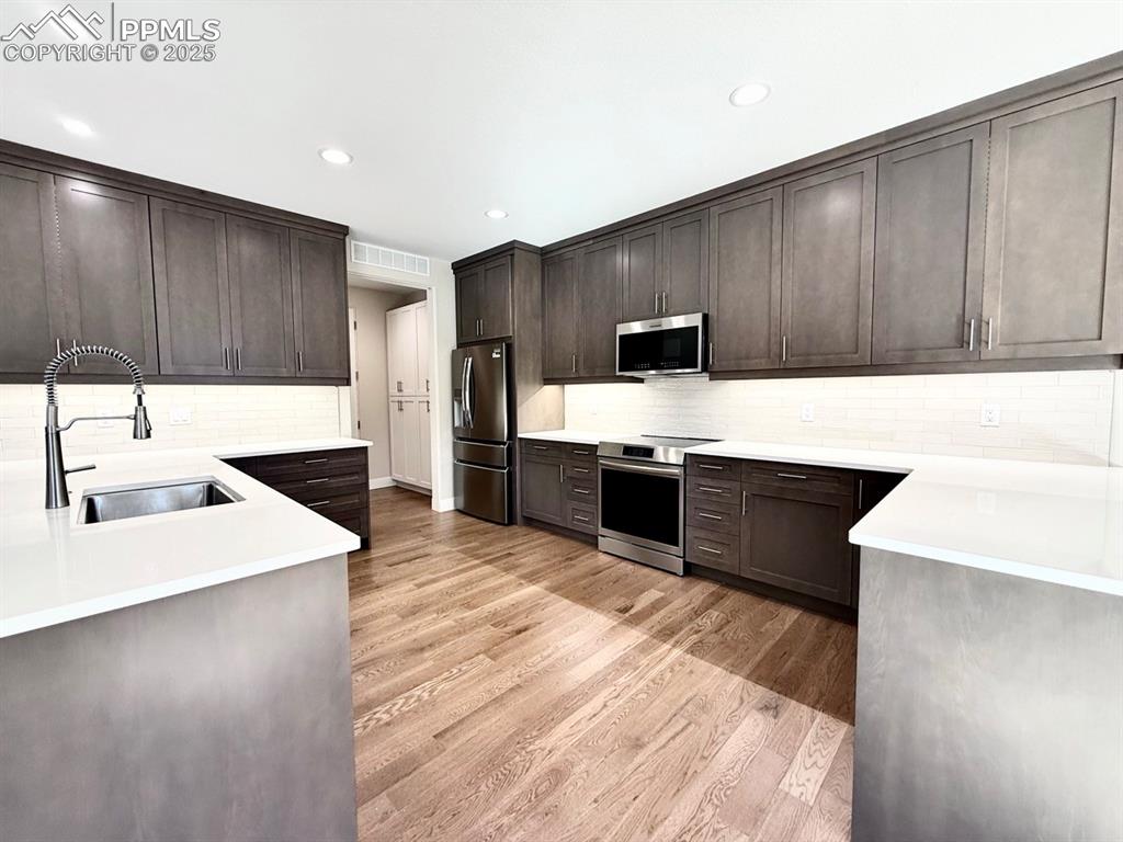 Full-sized Gourmet Kitchen with Quartz Countertops, Induction Range, Cabinetry to the Ceiling, Under-cabinet Lighting, Included Stainless Steel Fridge, and Wood Flooring.